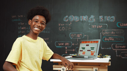 African boy using laptop programing system or coding prompt and turn around to smile to camera. Highschool student working learning to write engineering code while sitting blackboard. Edification.
