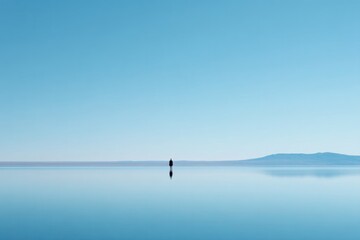 Fototapeta premium capture serene reflection of solitary figure standing by calm lake under clear sky