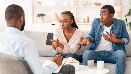 Jealous Wife. Angry Black Woman Showing Husband's Phone To Counselor, Blaming Him For Cheating And...