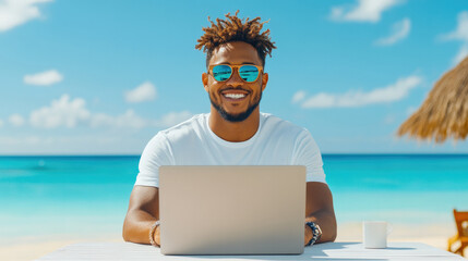 Young man smiling while working on laptop at beach with clear blue sky relaxed remote work concept