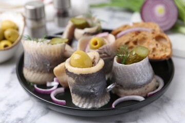 Delicious herring rolls with olives, pickles, dill, onion and bread pieces on light marble table, closeup
