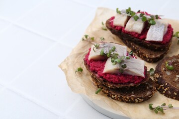 Tasty sandwiches with herring and horseradish sauce on white tiled table, closeup. Space for text
