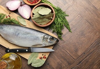 Salted herring, spices and knife on wooden table, flat lay. Space for text