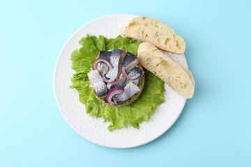 Delicious salad with herring, vegetables and bread on light blue background, top view