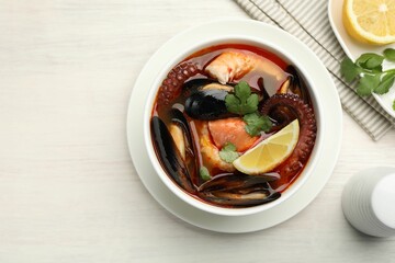 Delicious seafood soup in bowl, lemon and spices on light wooden table, flat lay. Space for text