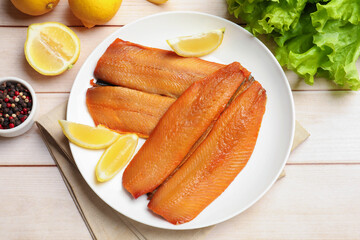 Delicious smoked herring fillets with lemon slices on white wooden table, flat lay