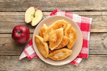 Delicious fried pyrizhky (stuffed pies) and apples on wooden table, flat lay