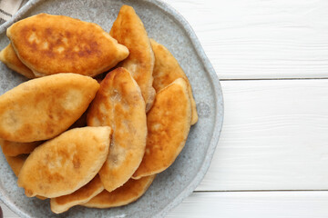 Delicious fried pyrizhky (stuffed pies) on white wooden table, top view. Space for text