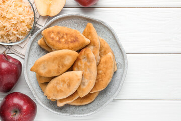 Delicious fried pyrizhky (stuffed pies) and apples on white wooden table, flat lay. Space for text
