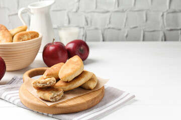Delicious fried pyrizhky (stuffed pies) and apples on white wooden table, closeup. Space for text