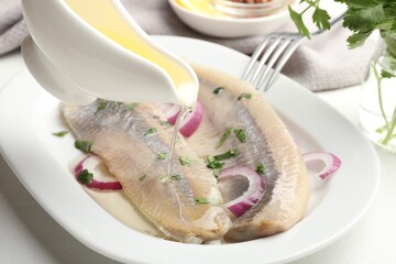 Pouring oil on tasty herring fillets with onions and parsley at table, closeup