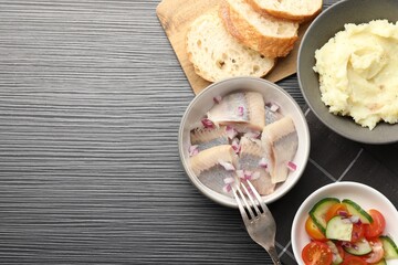 Delicious herring pieces with onions served on black wooden table, flat lay. Space for text