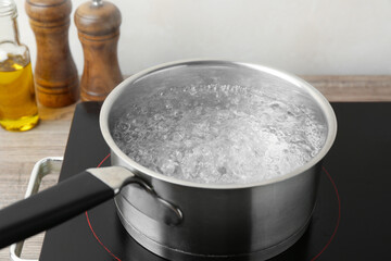 Saucepan with boiling water and stove on wooden table against white background, closeup
