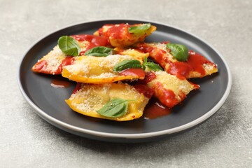 Delicious ravioli with tomato sauce, parmesan cheese and basil on grey table, closeup