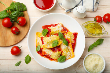 Delicious ravioli with tomato sauce, parmesan cheese and basil on white wooden table, flat lay