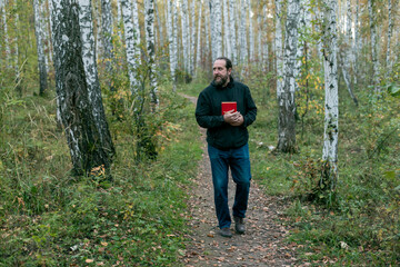 Fototapeta premium A man is walking through a forest with a red book in his hand