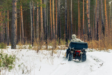 A man in camouflage is driving a four wheeler through a snowy forest