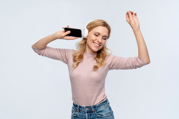 Fototapeta premium Photo of overjoyed lovely woman dressed casual outfit in headphones hand up listen music song using holding mobile phone isolated on white color background. Technology concept