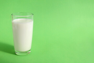 A glass of milk stands on a green background.