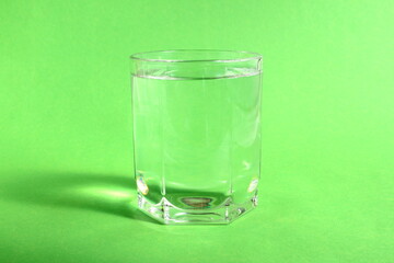 On a green background there is a glass cup with transparent clean drinking water.	