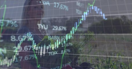 Mature woman holding green herbs in garden, overlaying finance candlestick charts and stock tickers