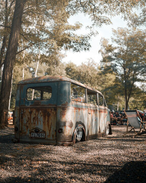 Rear view of vintage DKW Schnellaster van with weathered patina and lowered suspension parked on gravel during a classic car event &ndash; nostalgic retro vehicle scene in forested outdoor setting