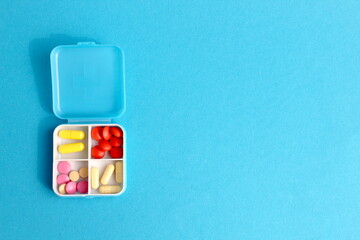 On a blue background lies a pill container with four compartments containing medicine.	