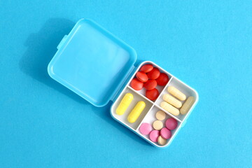  On a blue background lies a pill container with four compartments containing medicine.
