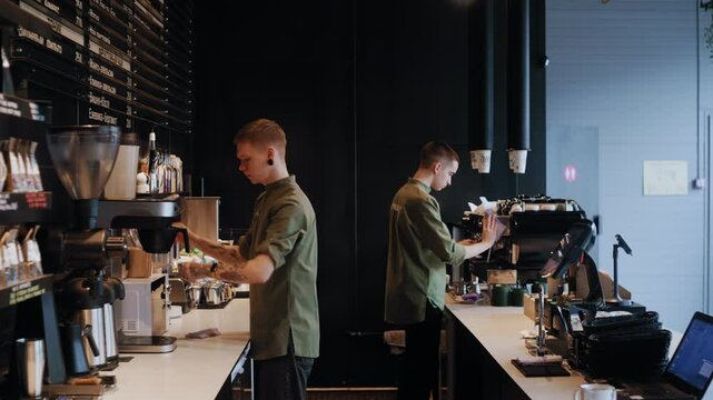Two baristas work side by side in a modern coffee shop, wiping equipment and cleaning surfaces during the morning opening preparations