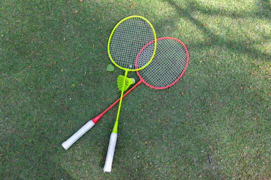 A pair of badminton rackets laid on fresh green grass, ready for an impromptu outdoor match and capturing the essence of summer play