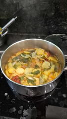 Traditional Portuguese codfish stew, known as caldeirada de bacalhau, prepared in a stainless steel pot with sliced potatoes, onions, tomatoes, peppers, herbs and olive oil.Homemade meal on a stovetop
