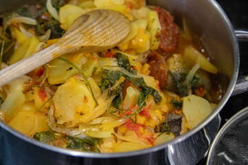 Traditional Portuguese codfish stew, known as caldeirada de bacalhau, prepared in a stainless steel pot with sliced potatoes, onions, tomatoes, peppers, herbs and olive oil.Homemade meal on a stovetop