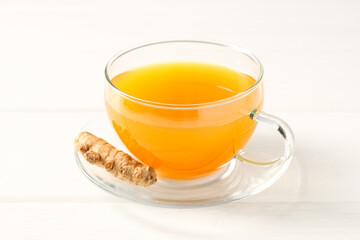 Aromatic turmeric tea in glass cup and root on white wooden table, closeup
