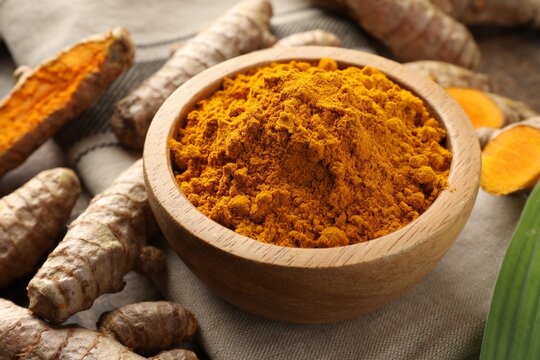 Turmeric powder in bowl and roots on table, closeup