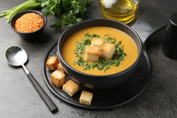Delicious lentil cream soup served with croutons on grey table, closeup