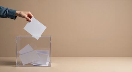 Hand casting a vote into a transparent ballot box against a plain background  