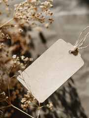 Minimal blank label tag mockup tied with string among dry flowers. Natural branding or handmade gift presentation template with rustic and organic aesthetic