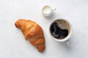Black americano coffee, coffee creamer and french croissant on a grey stone table background, top view
