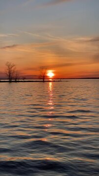 Sunset Over Lake with Silhouetted Trees and Reflected Sky, The sky reflects in the water while soft clouds