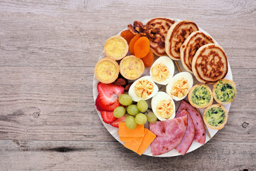 Breakfast or brunch grazing board. Assorted items including fruit, ham, quiche, pancakes and eggs. Top view on a wood background.