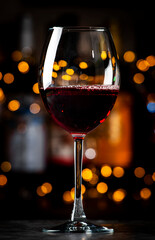 Italian dry red wine sangiovese in glass and wine bottles on dark bar background with lights