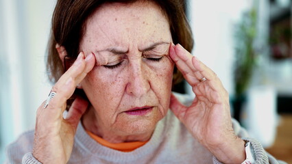 Mature woman enduring intense headache, eyes closed, hands on temples. Expression and facial lines...