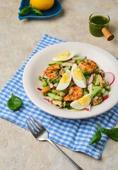 Salad of fresh cucumber, radish and eggs with seafood in a ceramic plate on a light concrete background. Salad recipes.