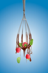 Chocolate cream dripping from whisk and falling raspberries on blue gradient background