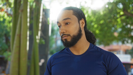 Young man with beard in urban park setting during daylight reflecting diverse culture and serene...