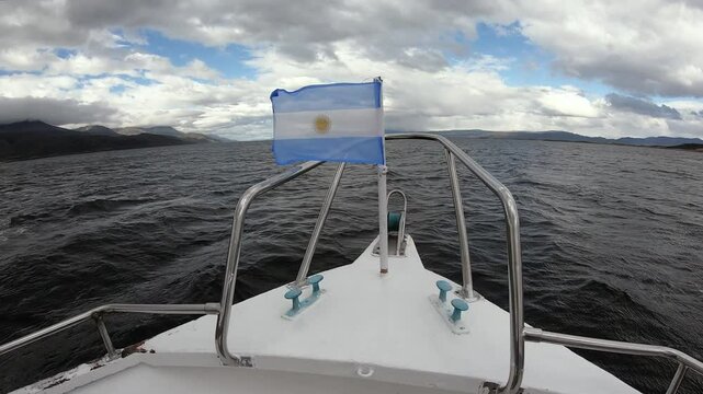 Navigating across the Beagle Channel under a majestic sky with clouds. View of the Argentinian flag blowing in the prow of the ship and the Andes mountains at shore