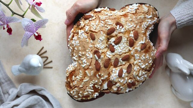 Woman hands serving Colomba pasquale or colomba di Pasqua  is an Italian traditional Easter bread or cake with almonds and raisins. Top view of table with flowers and easter bunny and bird.