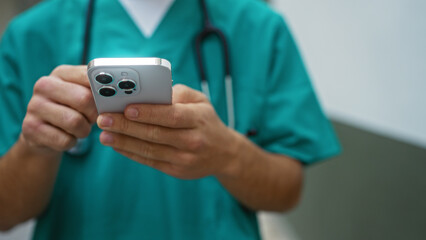 Medical professional using smartphone outdoors in urban setting, focusing on hands, technology, and stethoscope, suggesting healthcare communication in city environment.