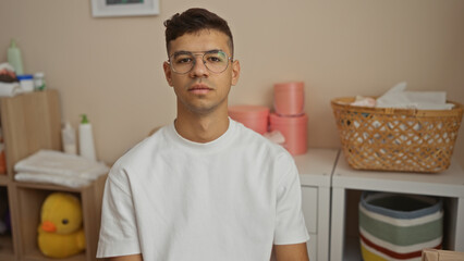 Young hispanic man with glasses in a casual setting at home looks confidently into the camera surrounded by cozy decor in a modern living room interior.