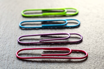 Colorful Metal Paperclips Arranged in a Line on Textured Grey Desk Surface